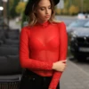 Long-sleeve red lace bodysuit with sheer mesh base and hook-and-eye closure, worn with dark denim.
