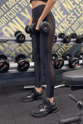 Black high-waisted microfiber leggings with a side mesh panel, side view in a gym setting